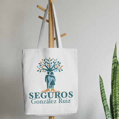 Tote bag with 'Seguros Gonzalez Ruiz' logo hanging on a wooden coat rack against a neutral background.